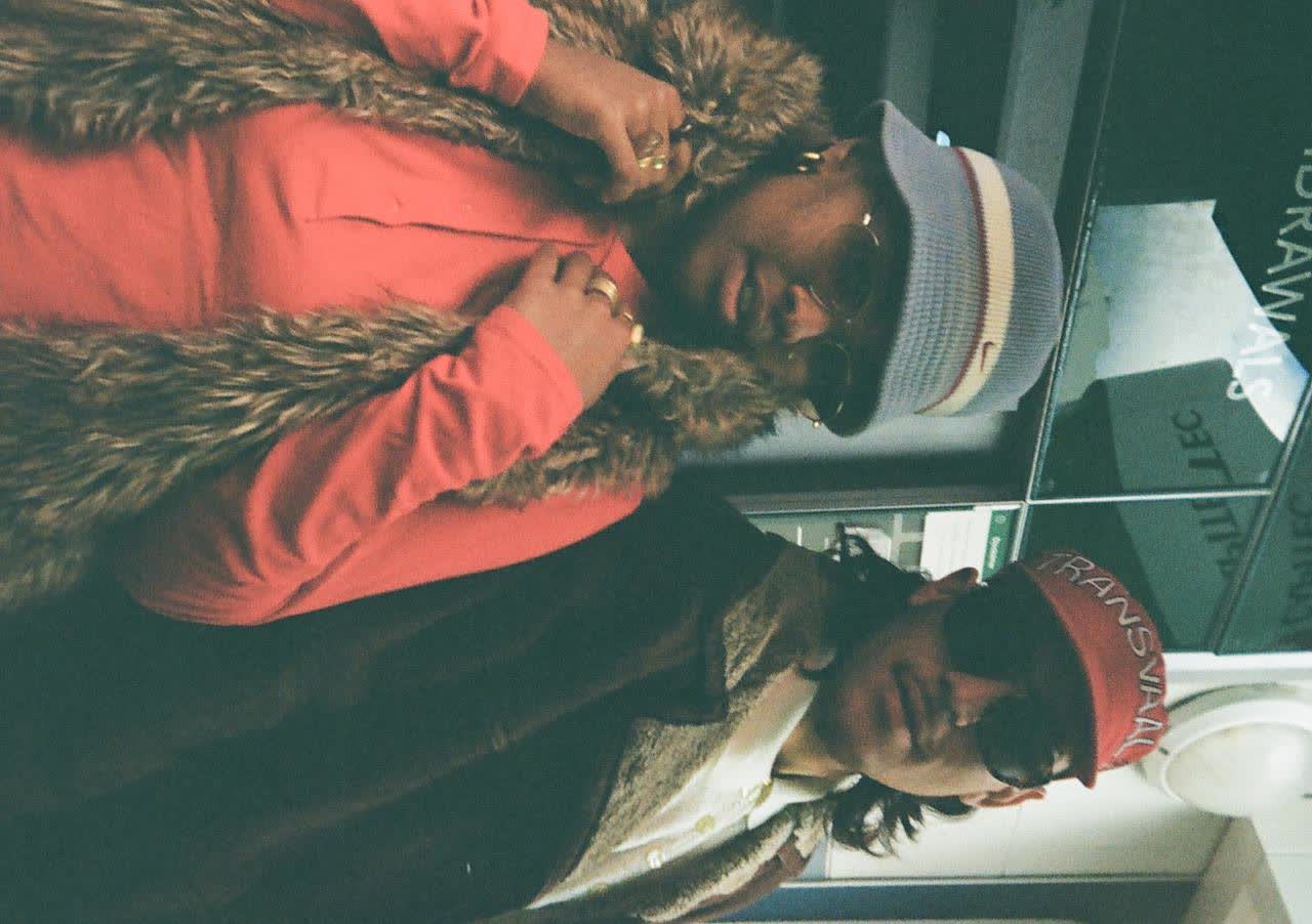 Close-up of two friends in a car, one in a red top with a fur collar
