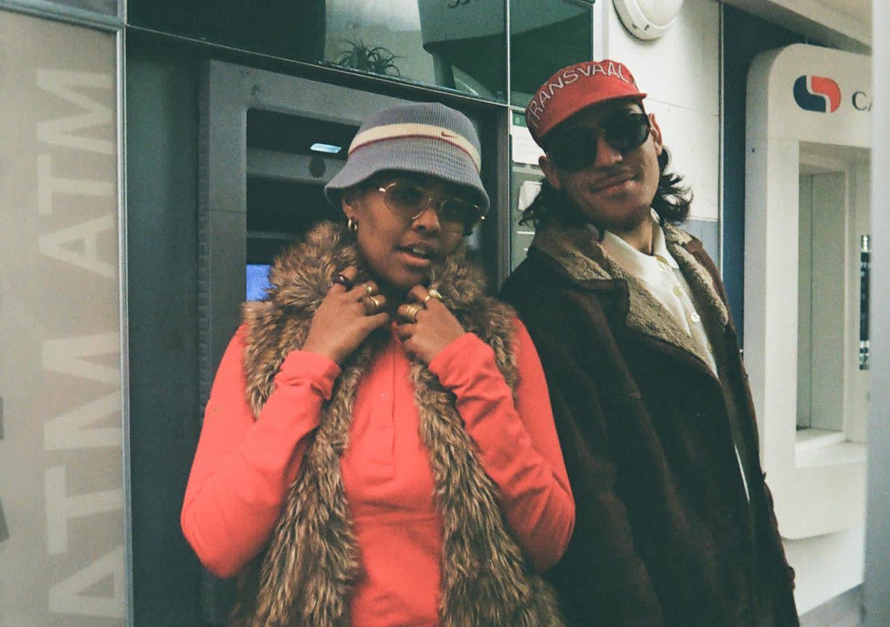 Two friends in thrifted fur-collar and knit layers outside the shop