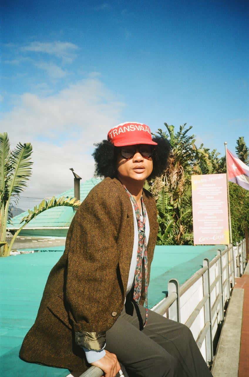 Person in a brown tweed coat and red cap standing beside a teal pool deck