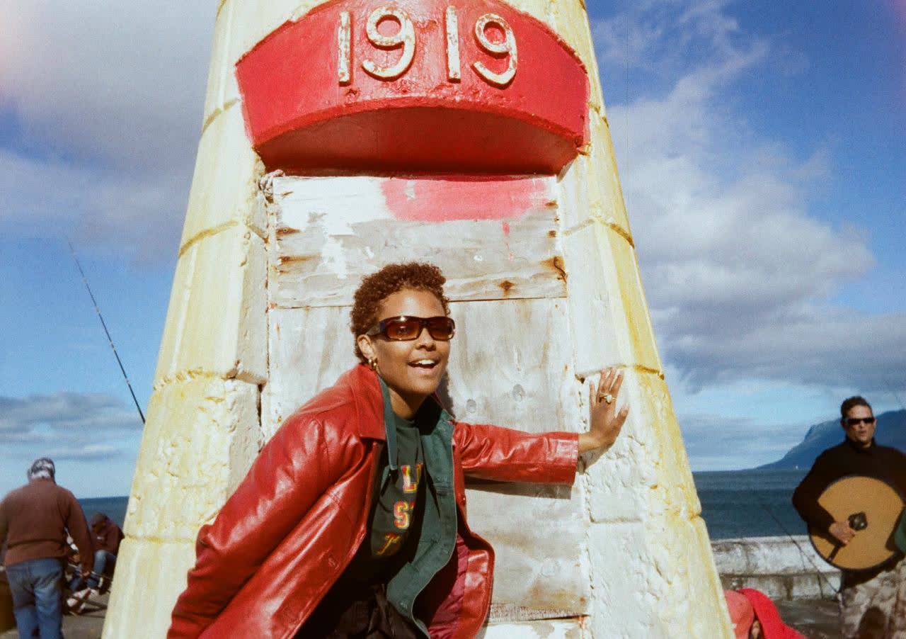 Woman in a red leather coat and sunglasses leaning against a painted 1919 monument
